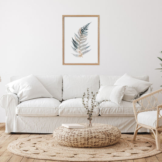Living room with a white sofa, woven ottoman, and framed plant art on the wall.