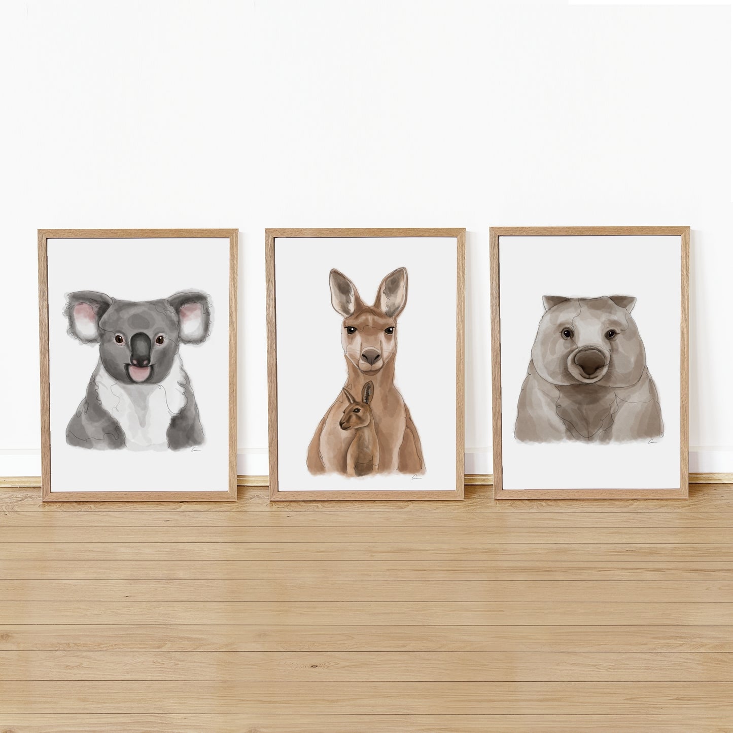 Three framed illustrations of a koala, kangaroo, and wombat on a wooden shelf against a white wall.