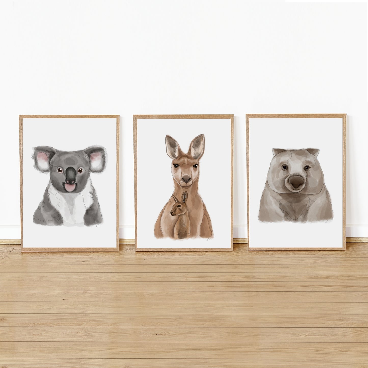Three framed illustrations of a koala, kangaroo, and wombat on a wooden shelf against a white wall.