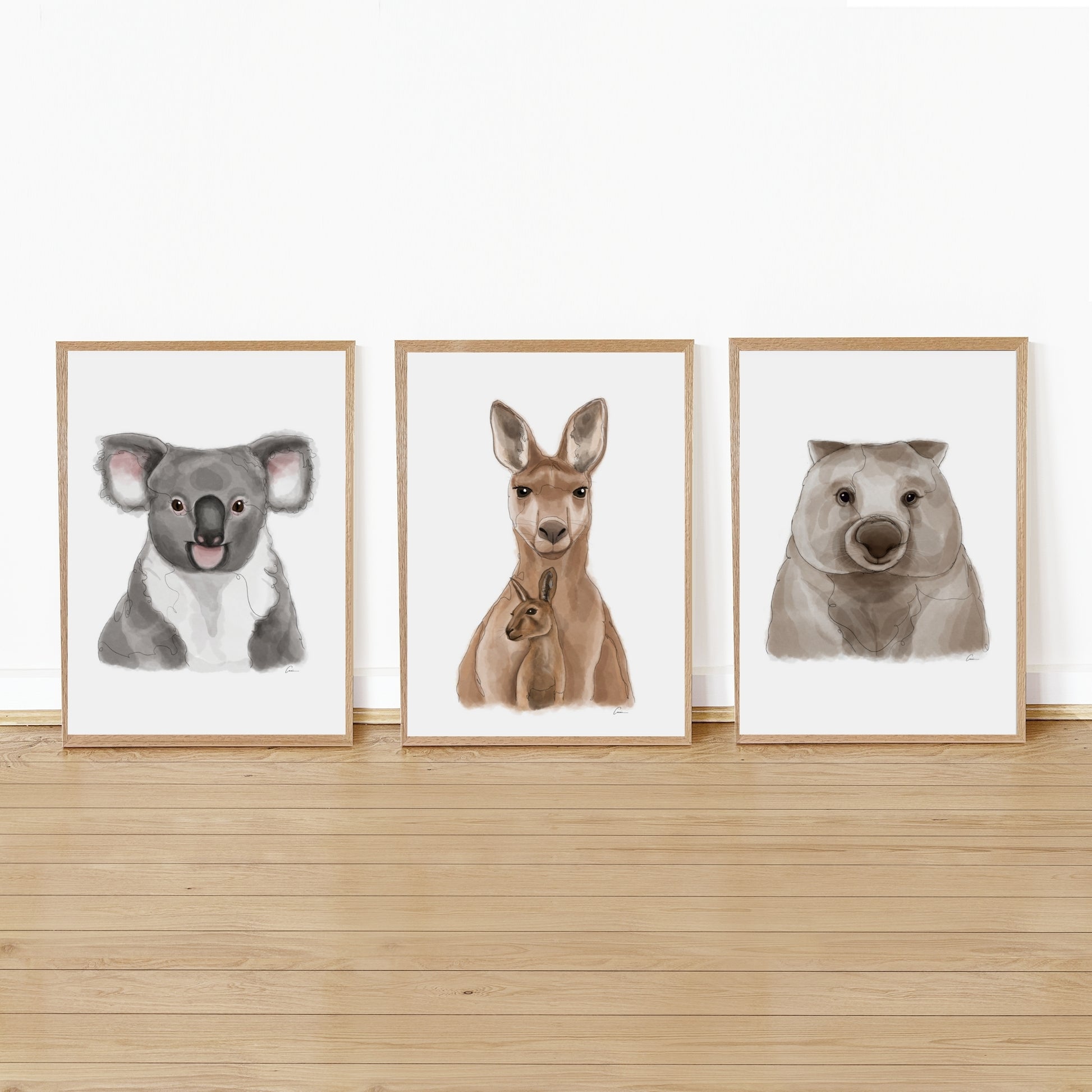 Three framed illustrations of a koala, kangaroo, and wombat on a wooden shelf against a white wall.
