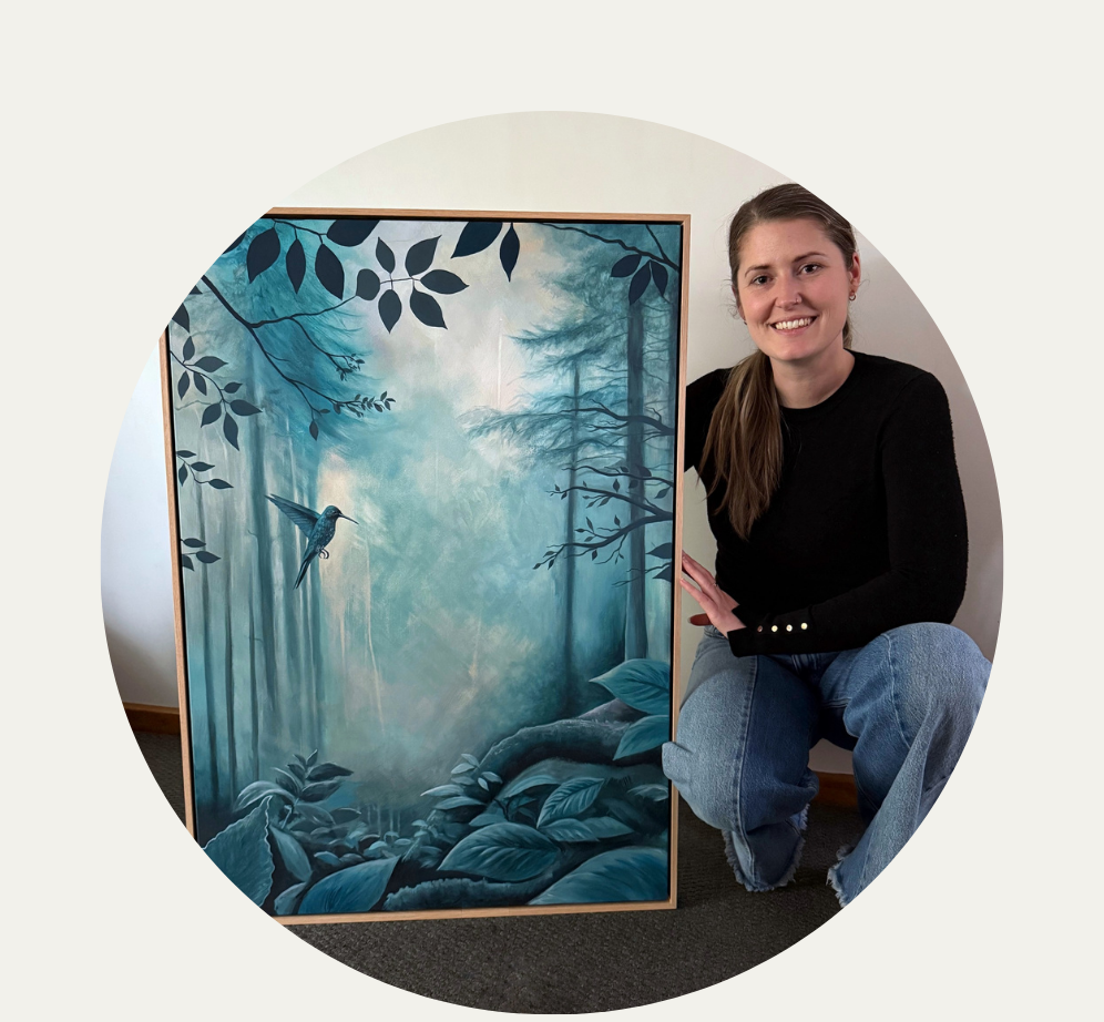 Person sitting next to a framed artwork of a forest scene with a bird.