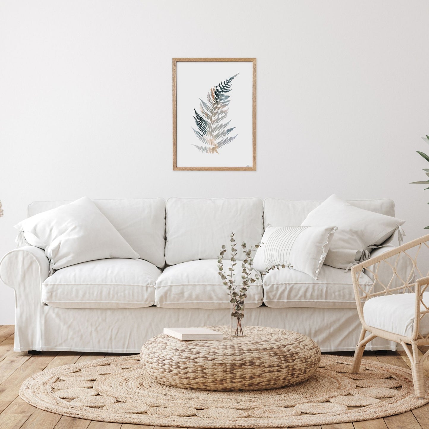Living room with a white sofa, woven ottoman, and framed artwork on the wall.